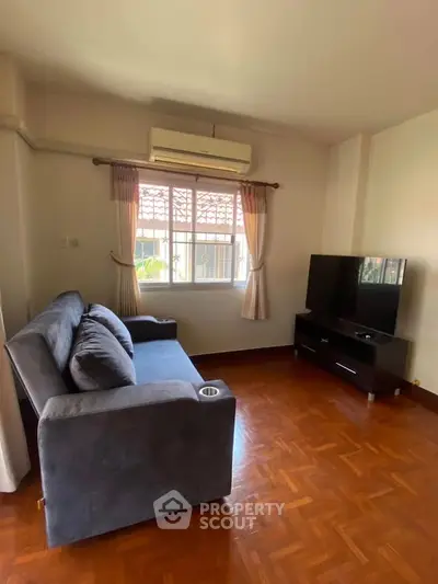 Cozy living room with modern sofa and flat-screen TV, featuring wooden flooring and natural light.