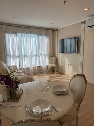 Elegant living room with dining area, featuring classic furniture and natural light through large windows.