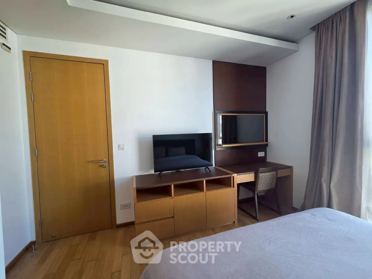 Modern bedroom with wooden flooring, TV, and desk setup, perfect for a cozy living space.