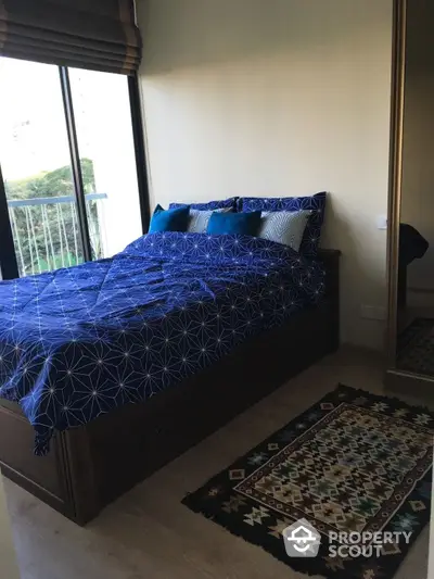 Cozy bedroom with a large bed adorned with blue bedding, floor-to-ceiling windows offering natural light, and a traditional rug adding a touch of elegance.