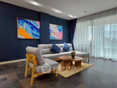 Modern living room with stylish furniture and vibrant artwork, featuring a cozy seating area and large windows.