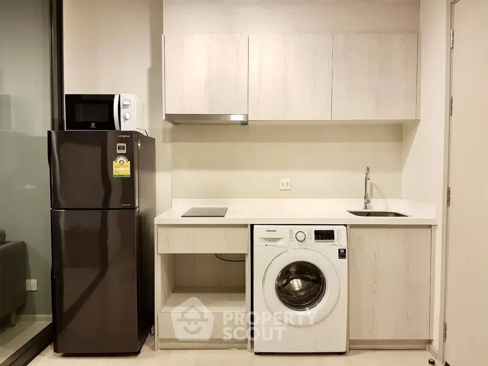 Modern kitchen with sleek appliances including fridge, microwave, and washing machine in compact layout.