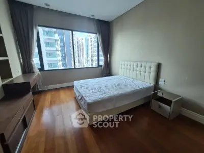 Spacious bedroom with large window offering city view, featuring a comfortable bed and wooden flooring.