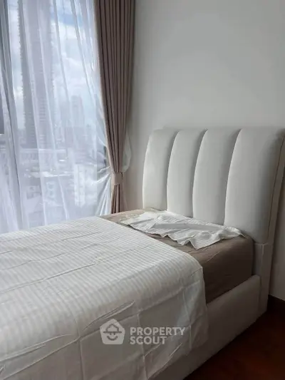Elegant bedroom with plush bed and city view through large window, perfect for urban living.