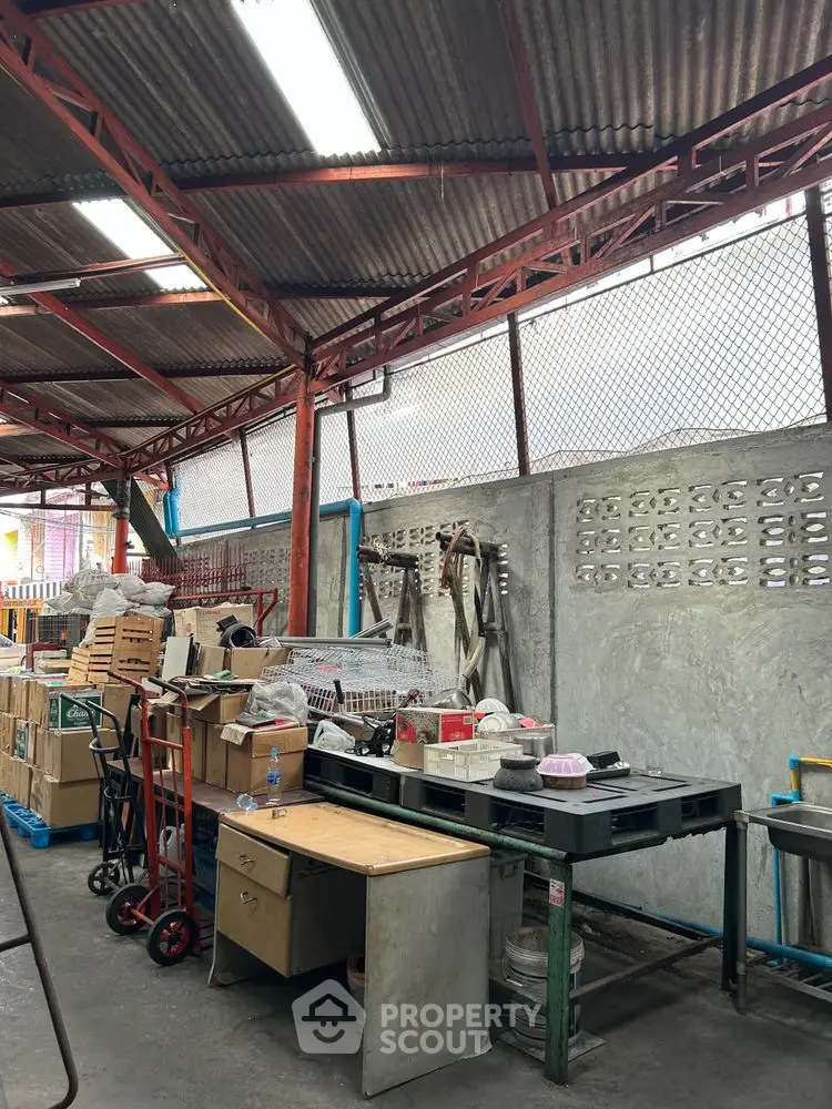 Industrial storage space with metal roof and concrete walls, featuring desks and storage equipment.