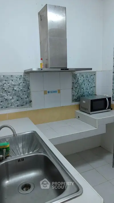 Modern kitchen with stainless steel sink and microwave, featuring sleek tiled backsplash.