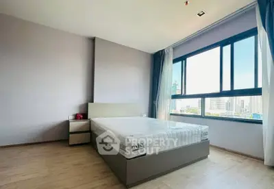Spacious bedroom with large window offering city views, modern furnishings, and natural light.