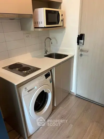 Compact kitchen with washing machine and microwave in modern apartment.