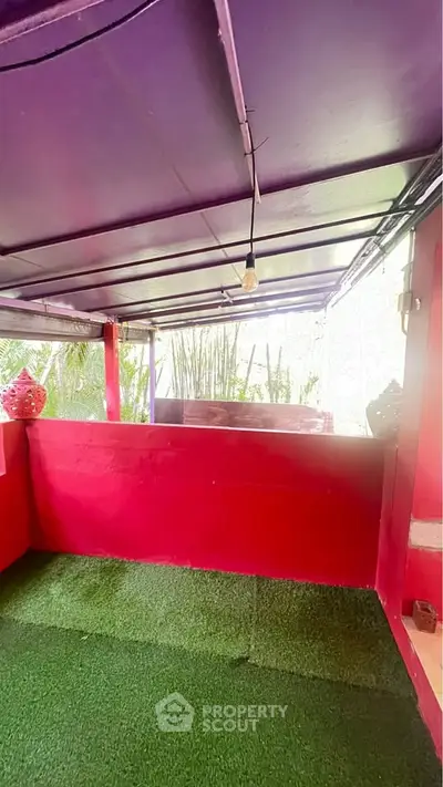 Charming outdoor balcony with vibrant red walls and lush greenery, perfect for relaxation and entertaining.