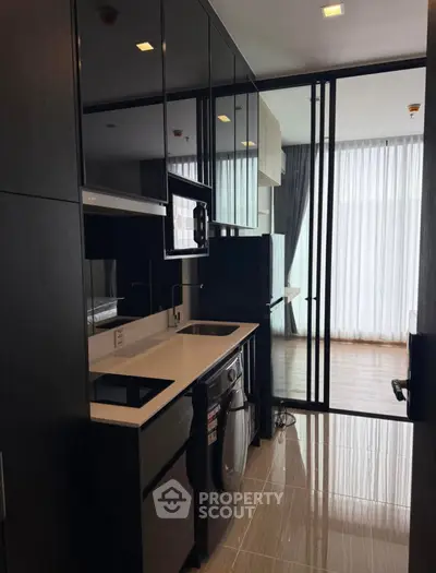 Modern compact kitchen with sleek black cabinets and integrated appliances in a stylish apartment.