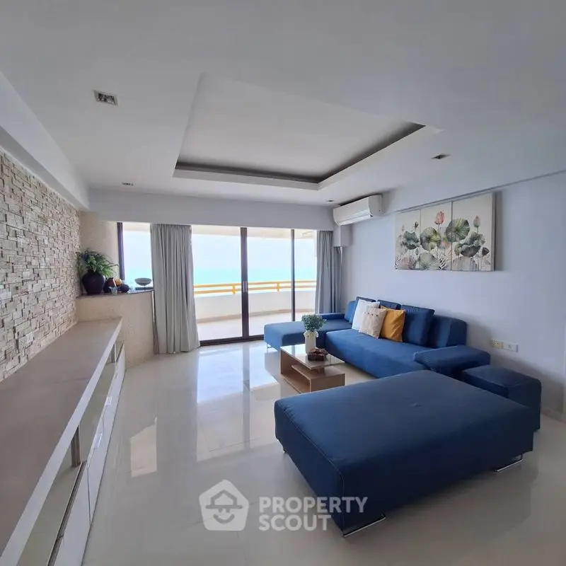 Spacious living room with modern blue sofa and large windows offering stunning ocean view.