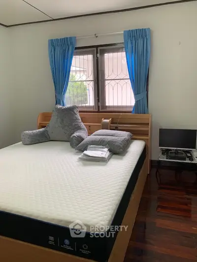 Cozy bedroom with wooden flooring, blue curtains, and a comfortable bed setup.