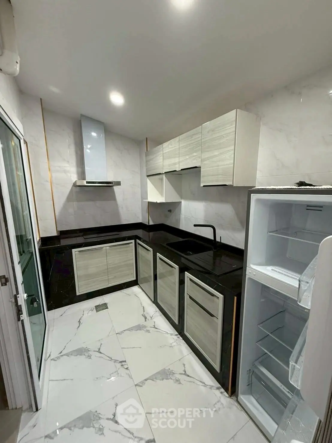 Modern kitchen with sleek black countertops and white cabinets, featuring a built-in fridge and marble flooring.
