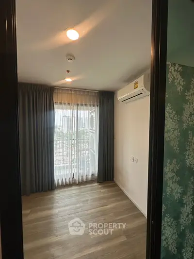 Spacious bedroom with wooden flooring and large window offering natural light and city view.