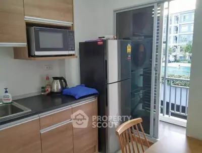 Modern kitchen with balcony view, featuring microwave and fridge in a cozy apartment setting.