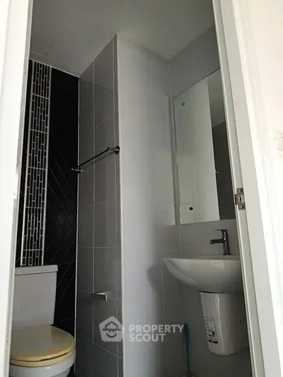 Compact modern bathroom with sleek black and white tiles, featuring a mirror and sink.