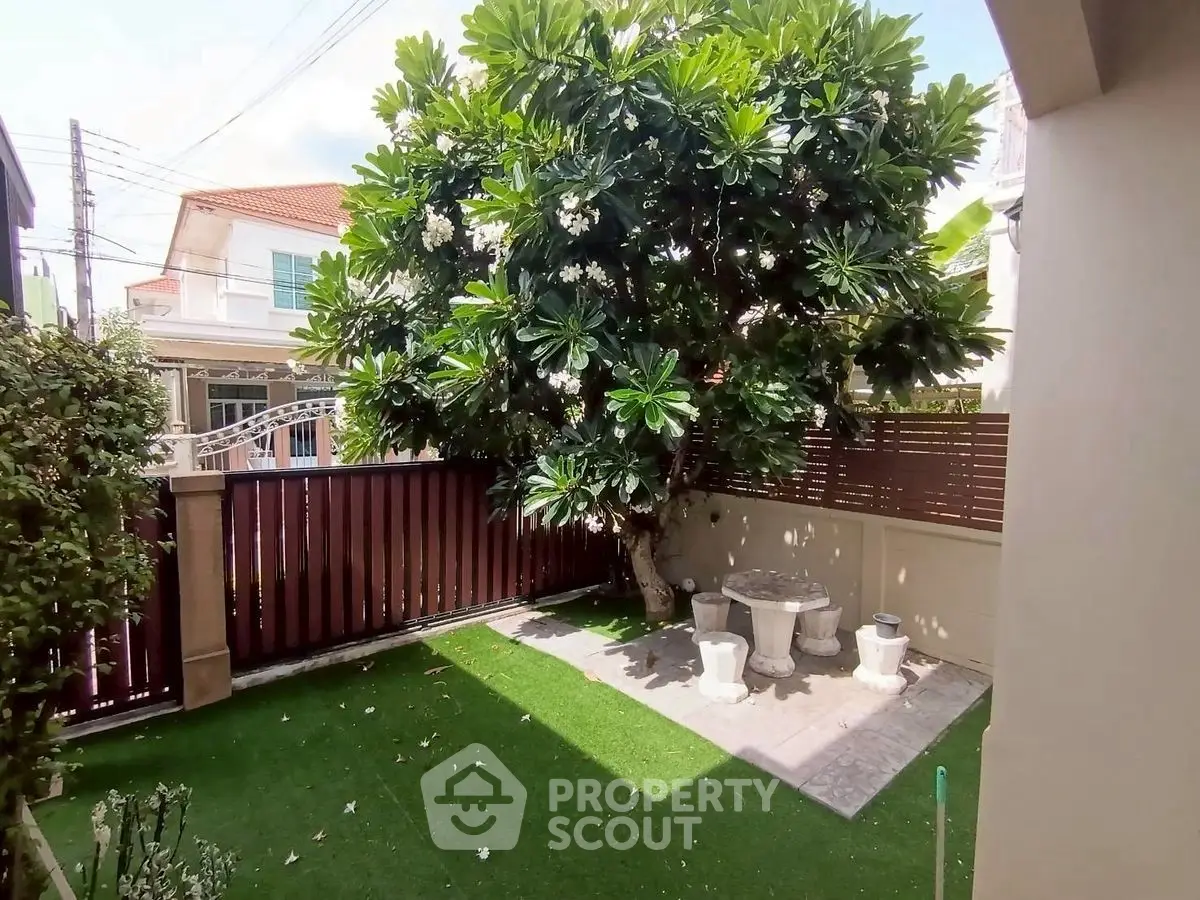 Charming garden with lush tree and cozy seating area in a serene residential setting.