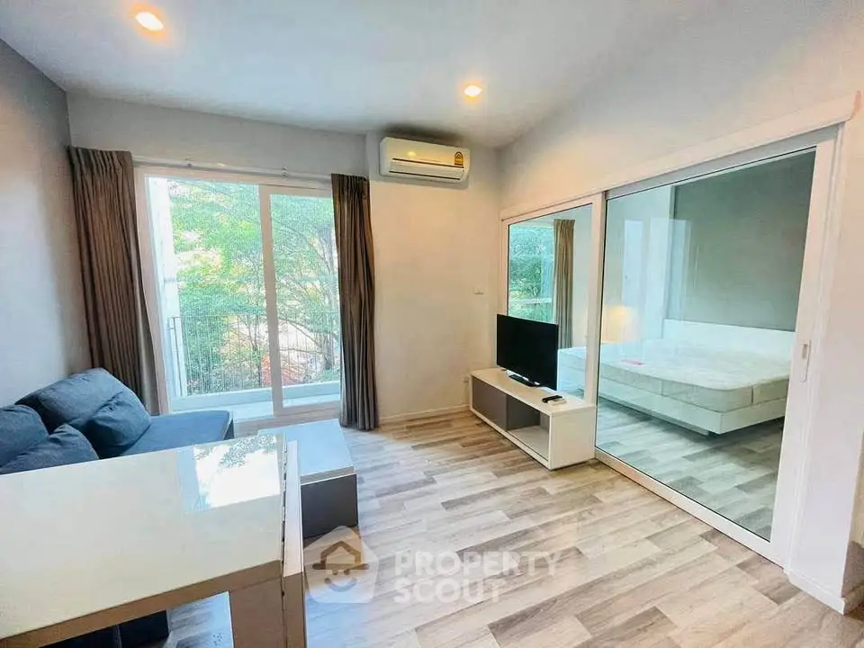 Modern living room with large windows and sliding glass doors, featuring a cozy sofa and sleek TV stand.
