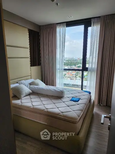 Modern bedroom with large window offering stunning city view, featuring elegant decor and natural light.