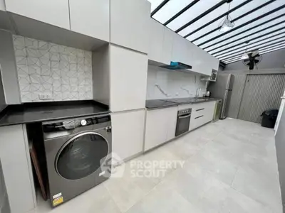 Modern kitchen with sleek appliances and open layout, featuring a washing machine and stylish backsplash.