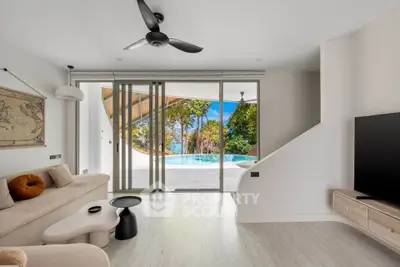 Luxurious living room with pool view, modern decor, and large sliding glass doors opening to a tropical paradise.