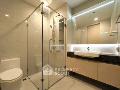 Modern bathroom with glass shower enclosure and sleek vanity in luxury apartment.