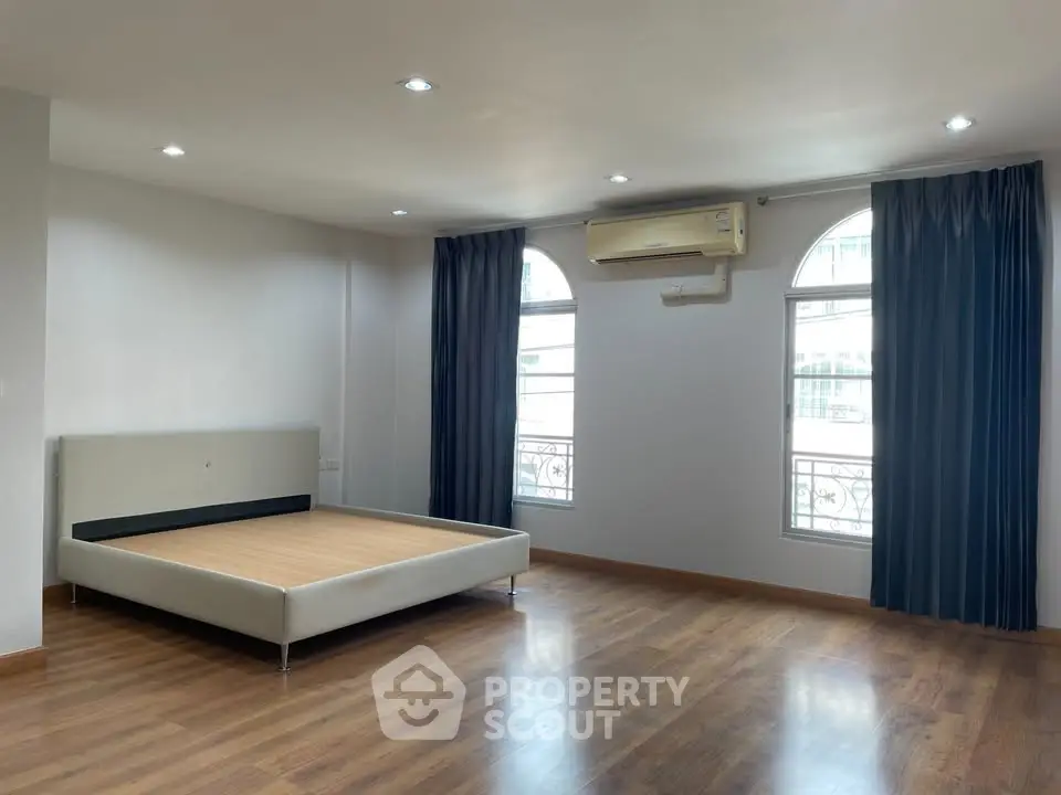 Spacious bedroom with wooden flooring and large windows for natural light