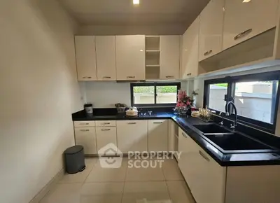 Modern kitchen with sleek white cabinets and black countertops, featuring large windows for natural light.