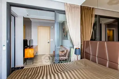 Modern bedroom with stylish decor and glass partition leading to living area.