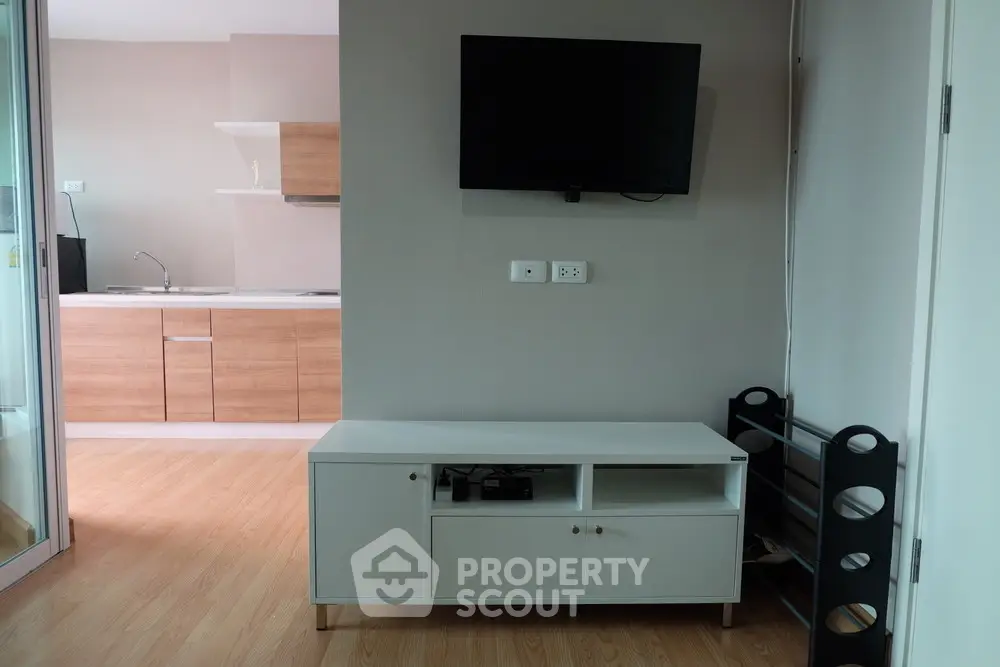 Modern living room with wall-mounted TV and sleek storage unit, adjacent to a minimalist kitchen.