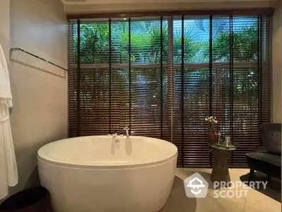 Luxurious bathroom with freestanding tub and garden view through wooden blinds.