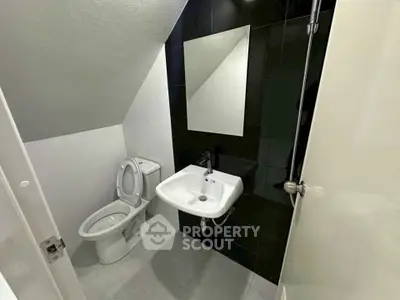 Compact modern bathroom with sleek black and white design under a sloped ceiling.