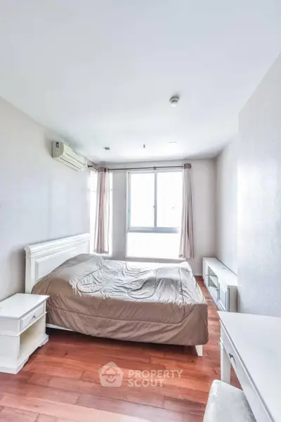 Spacious bedroom with wooden flooring and large window for natural light.