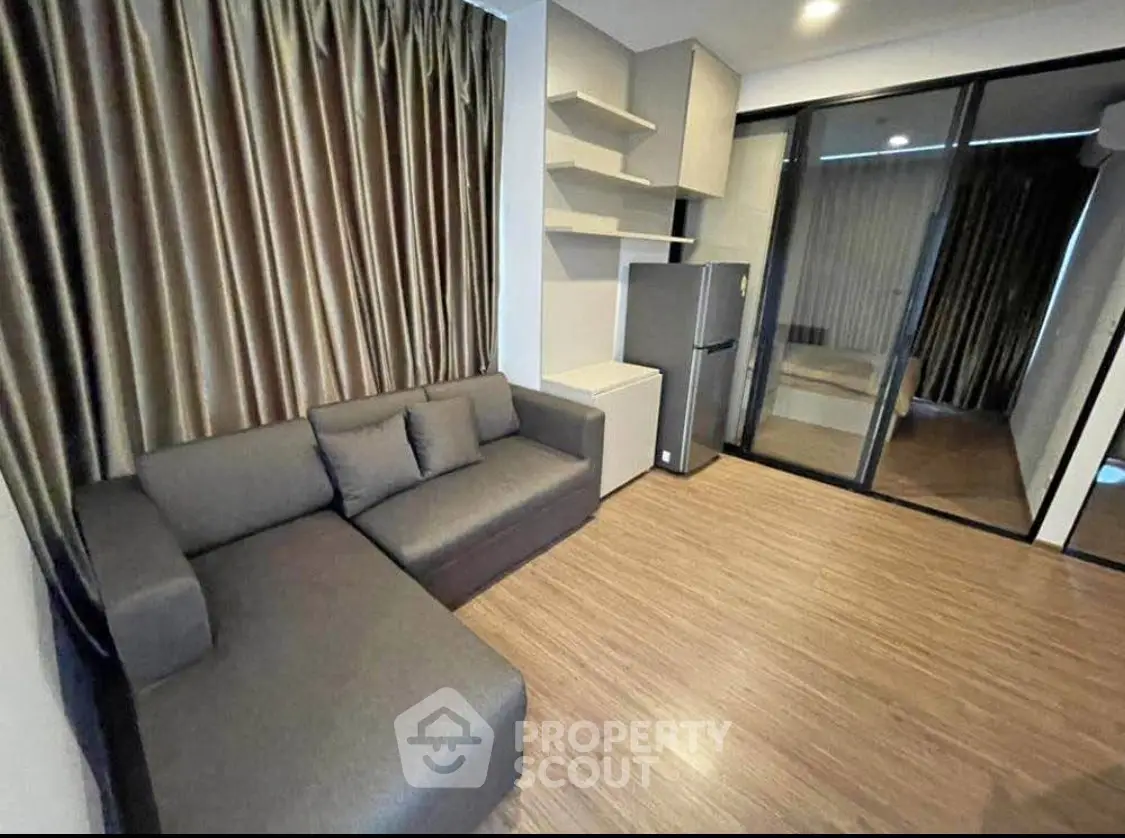 Modern living room with sleek sofa and fridge, featuring elegant curtains and wooden flooring.
