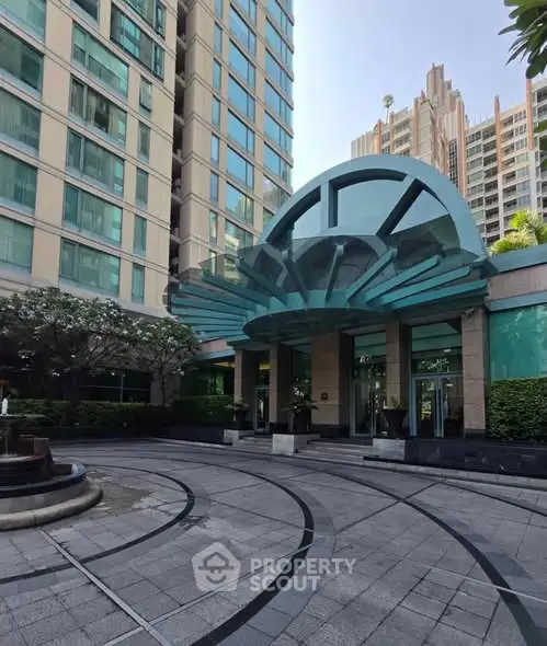 Elegant building entrance with modern glass canopy and landscaped surroundings.