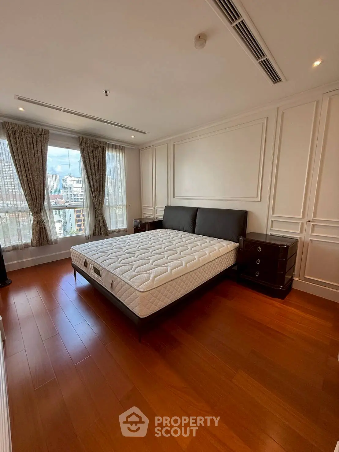 Spacious bedroom with elegant design and city view, featuring hardwood floors and large windows.