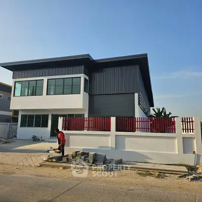 Modern two-story house with sleek design and red accents under clear blue sky.