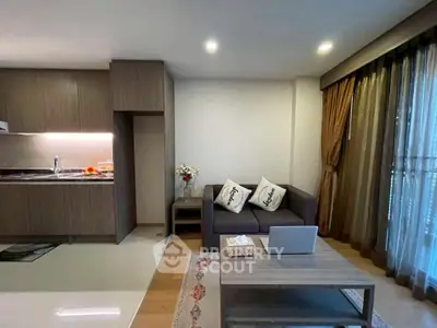 Modern living room with open kitchen, cozy sofa, and natural light from large windows.