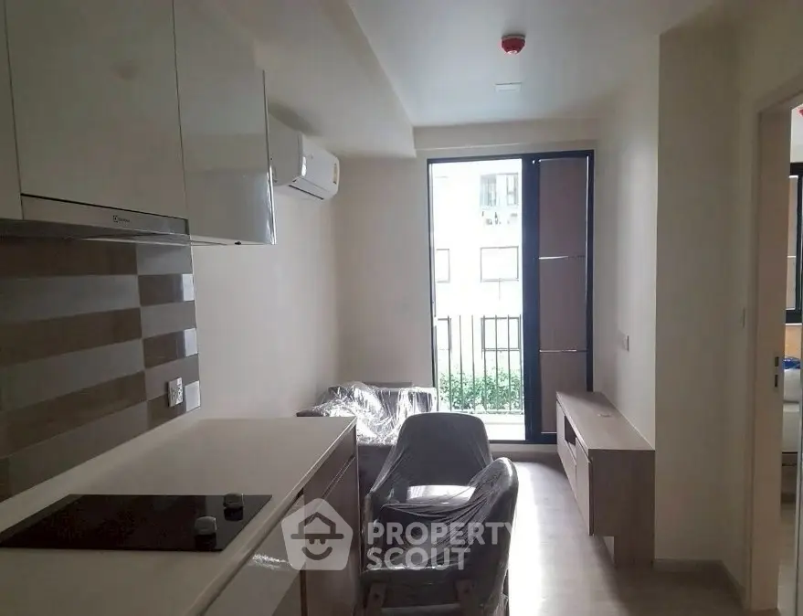 Modern apartment living room with sleek kitchen and balcony view, featuring contemporary furnishings.