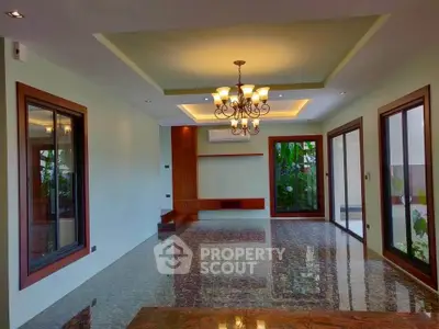 Spacious living room with elegant chandelier and large windows overlooking lush greenery.