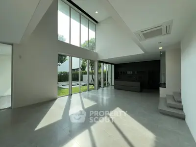 Spacious modern living room with high ceilings and large windows overlooking a garden.