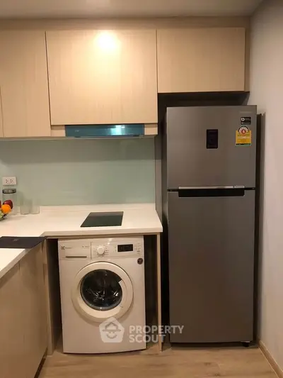 Modern kitchen with integrated washing machine and sleek refrigerator in compact layout.