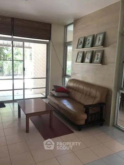 Cozy living room with leather sofa and wall art, featuring large windows and garden view.