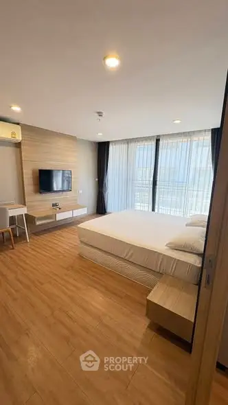 Modern bedroom with wooden flooring, large window, and wall-mounted TV in a stylish apartment.
