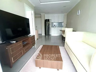 Modern living room with sleek furniture and open kitchen layout, featuring a large TV and stylish decor.