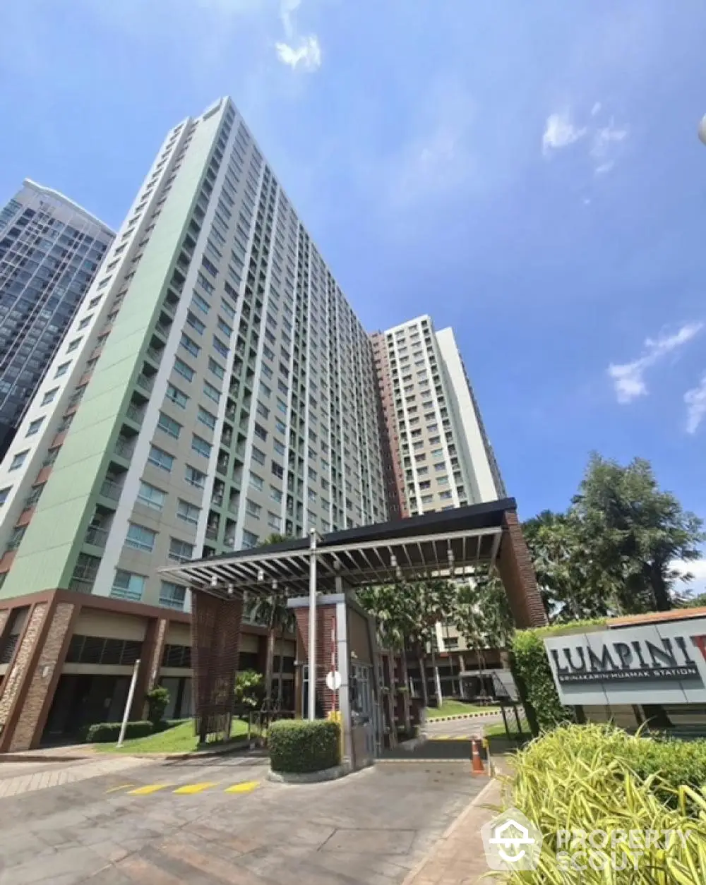 Modern high-rise condominium building with lush greenery and clear blue sky.