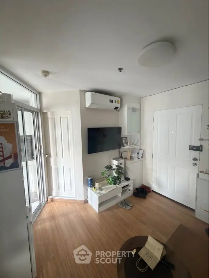 Modern living room with wooden flooring, wall-mounted TV, and air conditioning unit.