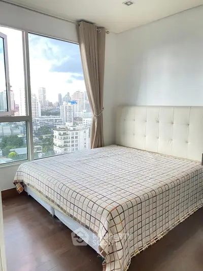 Bright bedroom with large window offering stunning city views, featuring a cozy bed and elegant curtains.