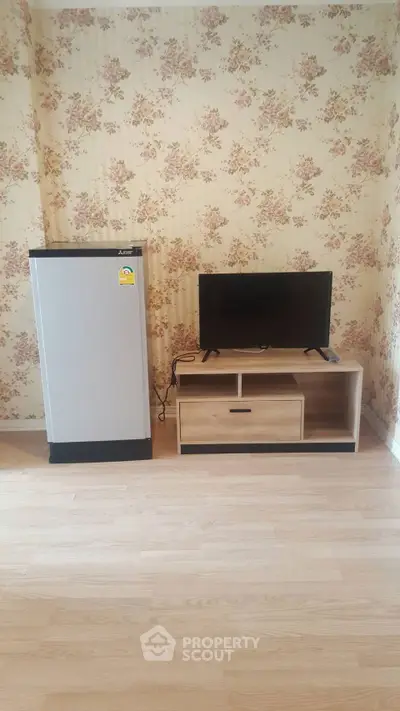Cozy living room with floral wallpaper, compact fridge, and TV stand for modern living.