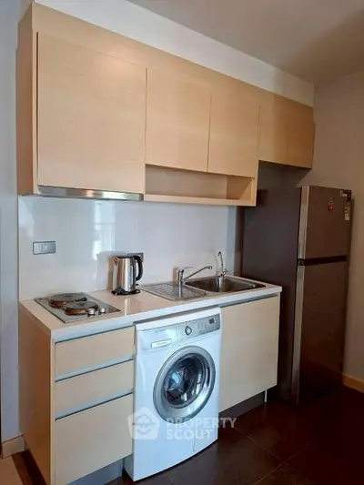 Modern kitchen with washing machine, fridge, and sleek cabinetry in compact layout.